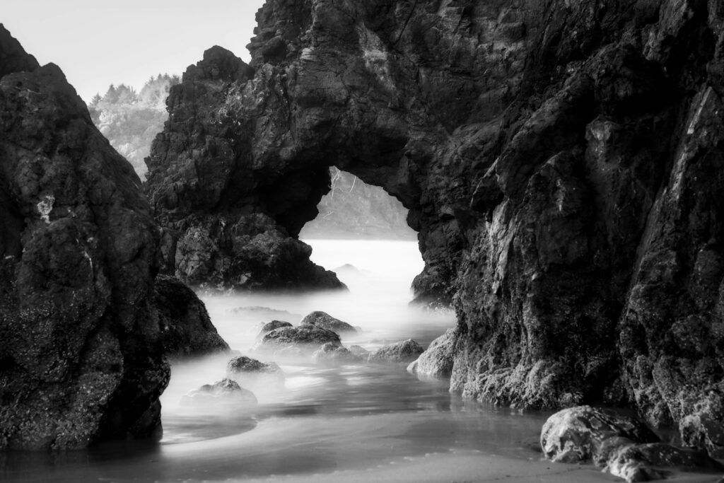 Rocky archway on a misty coastline with ocean waves